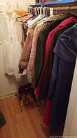 Closet full of vintage women's clothing, mostly outerwear and dresses hanging on hangers with shoes at the bottom