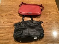 Top view of both purses on table, black larger tote purse and smaller strawberry red crossbody purse with visible carrying strap.