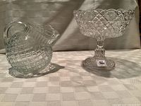 View of antique pressed glass pitcher and button and daisy pattern pedestal bowl showing clear glass and pattern details.