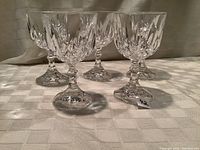 Five crystal water goblets arranged in a group on a white checkered tablecloth, showing clear cut crystal design and faceted stems.