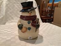 Full view of the ceramic snowman cookie jar with black top hat, maroon scarf, blue heart buttons, holding a stick and fan-shaped decoration.