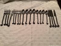 20 pieces of cutlery including forks, spoons, and knives laid out in a row showing the curled handle design.