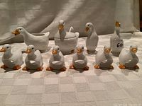 Front view of the full set including the duck creamer, sugar bowl, salt and pepper shakers, and six small duck napkin rings arranged on a cloth surface.