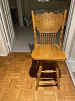 Front view of one solid oak swivel bar stool showing seat, legs, and carved decorative backrest detail.