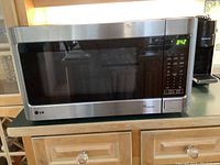 Front view of LG stainless steel microwave closed, showing digital control panel and clock display.