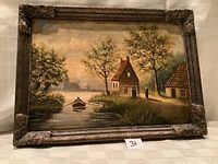 Full view of oil painting showing riverside scene with cottages, trees, boat, and figure, in an ornate carved frame.