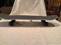 Side view of skateboard showing black grip tape and classic double-kick deck shape with wheels attached