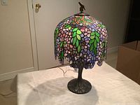 Full view of the stained glass lamp showing the leaf pattern and scalloped edges on the glass shade, with the metal base.