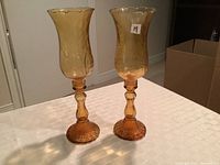 Two amber hurricane lamps displayed on a table, showing full height and detailing.