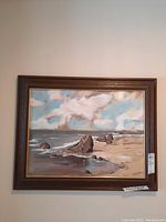 Photo of framed acrylic painting showing coastal scene with rocks, ocean, sky, and sandy beach, labeled with price tag.