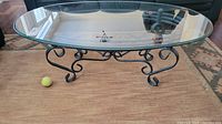 Oval beveled glass top showing clear transparency and smooth edges, resting on black metal scrollwork base.
