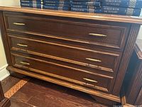 Front view of the wooden dresser showing three drawers and brass handles, minor scuff on top edge visible.