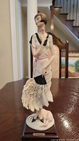 Full view of the 13-inch tall porcelain figurine by Guiseppe Armani showing woman with a fan and small dog on base.