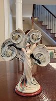 Front and full figurine photo showing the woman in white gown with large abstract fan shapes behind.