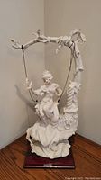 Full view of the porcelain lady on swing figurine with wood base on a wooden surface.