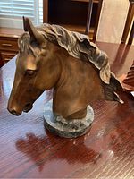 Front and left side view of copper horse head bust showing detailed mane and facial features, mounted on round stone base.