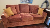 Front view of three-seat brown upholstered sofa with three seat cushions and two mustard accent pillows