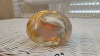 Side view of the amber-tinted art glass paperweight showing the swirl inside and surface details.