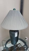 Photo of one pottery table lamp showing smooth vase-shaped mottled green base with a light-colored pleated fabric shade and green finial on top.
