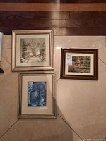 Three framed prints laid out on floor including bathroom interior, forest landscape, and pottery still life