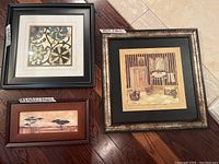 Photo of three framed prints on tile floor showing different designs, sizes, and frames.