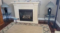 Wide view showing both side tables flanking a white fireplace, placed on wooden floors with decorative rugs.