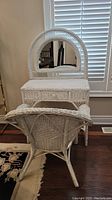 Front view of white wicker vanity with oval removable mirror and matching chair placed in front