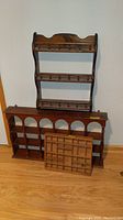 Three wooden wall display shelves stacked against a wall on a wooden floor. Includes a tall shelf with dowel pegs, a wider shelf with arched compartments, and a smaller grid shelf.