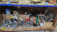 Photo of assorted bicycle parts including sprockets, cables, seats, and small tools inside wooden boxes and a shelf.