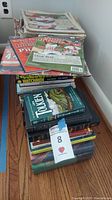 A wide shot showing stacked books, magazines, and sports newspapers like Watchmen, Tolkien, and Harry Potter titles with some 2008 Phillies memorabilia on top.