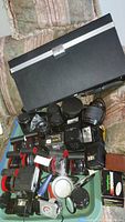 Lot showing a variety of vintage camera lenses, lens cases, and accessories in a black carrying case on a sofa.