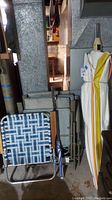 Three cloth covered folding beach chairs stacked, showing blue and white woven fabric and metal frames with wooden armrests, alongside two folded striped fabric patio umbrellas