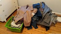 Overall lot showing green basket containing various clothing items including blazers, jeans and scarves on floor.