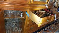 Open wooden drawer filled with assorted cutlery including knives and metal skewers alongside a metal sharpener tool