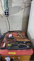 Overview of the lot showing assorted knives, razor blade packs, and a paper cutting board on a red cabinet.