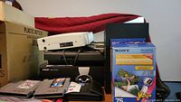 Photo showing stacked electronics including Philips audio receiver, Sony Picture Station box and paper, game cartridges, and cables.