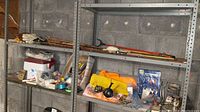 Metal shelving unit with fishing rods, lures, cooler, gloves, and miscellaneous accessories