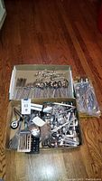 Overview of box with sets of flatware and various kitchen utensils on wooden floor
