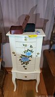 Jewelry armoire front view showing floral painted drawers and curved legs.