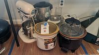 Full view showing KitchenAid mixer, two slow cookers including Daisy Dipper and Sultan with dent, food processor, and West Bend coffee pot.