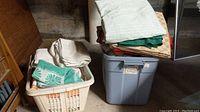 Two plastic containers filled with assorted linens including towels, placemats, and fabric pieces.