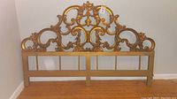 Full front view of carved wood look headboard with ornate scroll and floral design, showing overall shape and detailing.