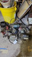Overview of several electric motors and some metal parts on a floor with a yellow bin in the background.
