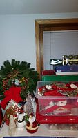 Wide view showing Christmas wreath, Santa and snowman figurines, and stacked plastic bins with assorted ornaments.