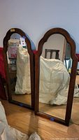 Pair of two wood framed mirrors standing side by side on floor, showing full height and frame detail.