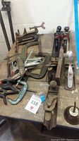 Wide view of all planes and clamps on wooden table including multiple C-clamps, 6 planes, and hand clamps.