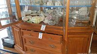 Wooden cabinet with glass front containing porcelain and glass items, view of top shelf showing teapots and bowls