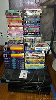 Magnavox VHS player, Sony DVD player, stacks of VHS tapes including movies and workouts, and sealed blank Sony VHS tapes.