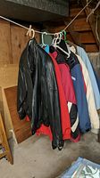 Four vintage coats hanging on clothesline in basement setting: black leather jacket, red insulated coat, blue insulated coat, and cream white insulated coat.