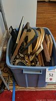 Blue plastic storage bin filled with assorted framed prints and decor items stacked vertically and horizontally.